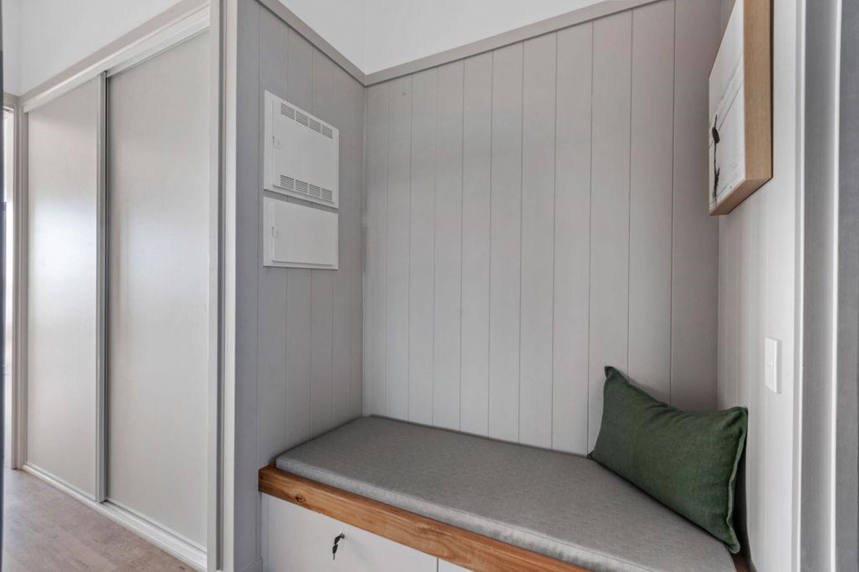 A corner room with a built-in bench, a small cabinet, and a wall-mounted air conditioning unit.