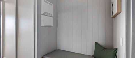 A corner room with a built-in bench, a small cabinet, and a wall-mounted air conditioning unit.