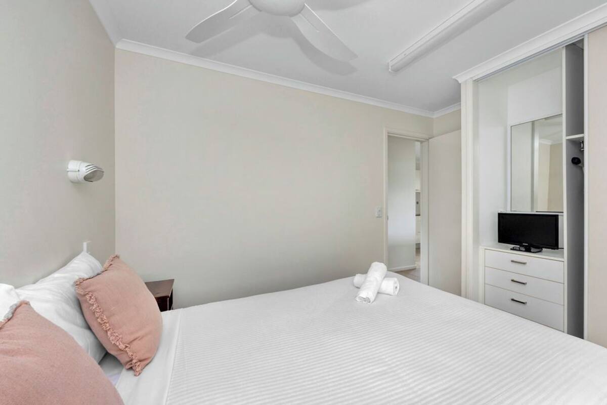 A hotel room with a bed, a television on a dresser, and a ceiling fan.
