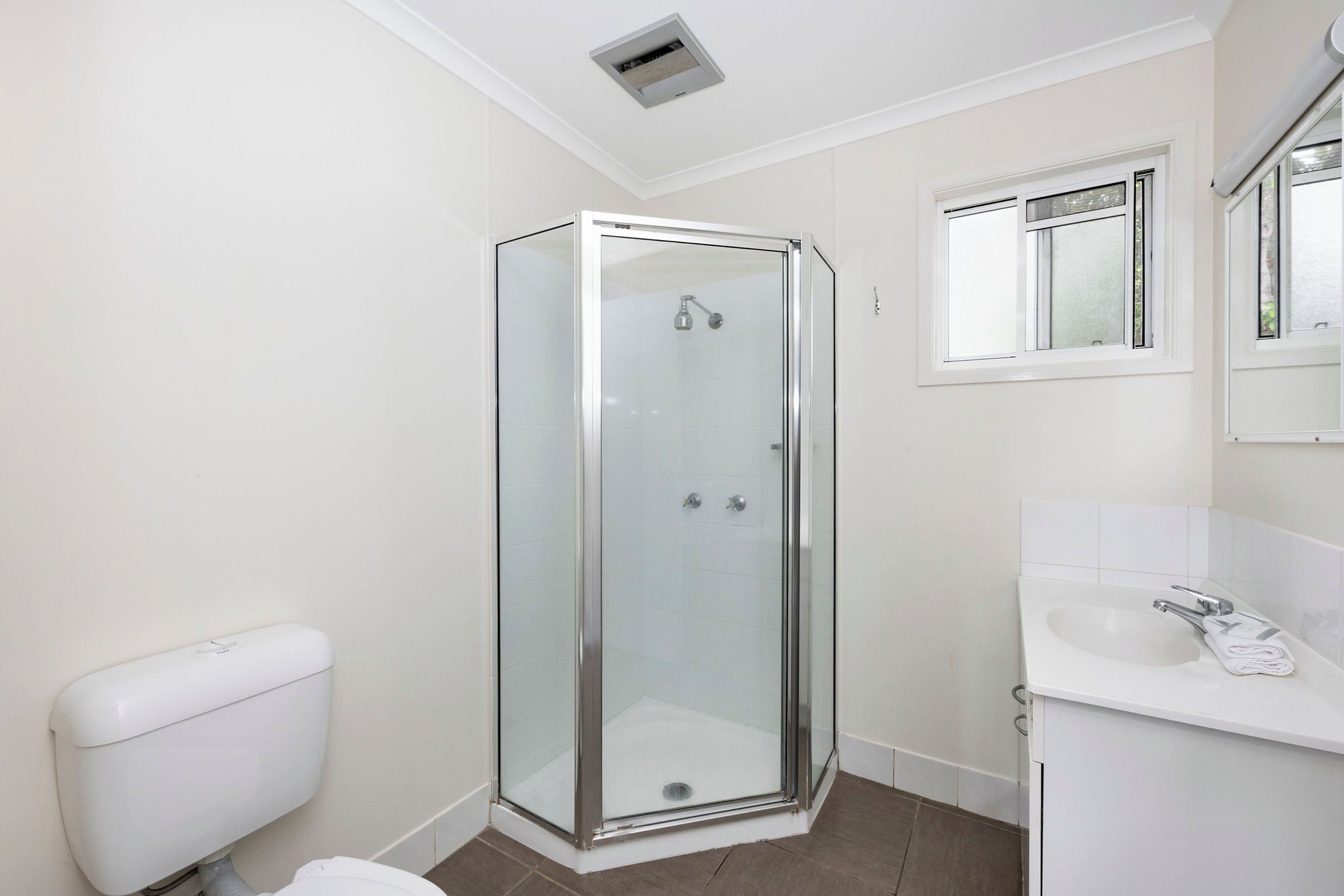 A modern bathroom with a glass-enclosed shower, a white sink, and a toilet.