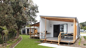 A modern, minimalist house with a wooden deck and a covered outdoor seating area. - Reflections Urunga - Holiday Park (Urunga)