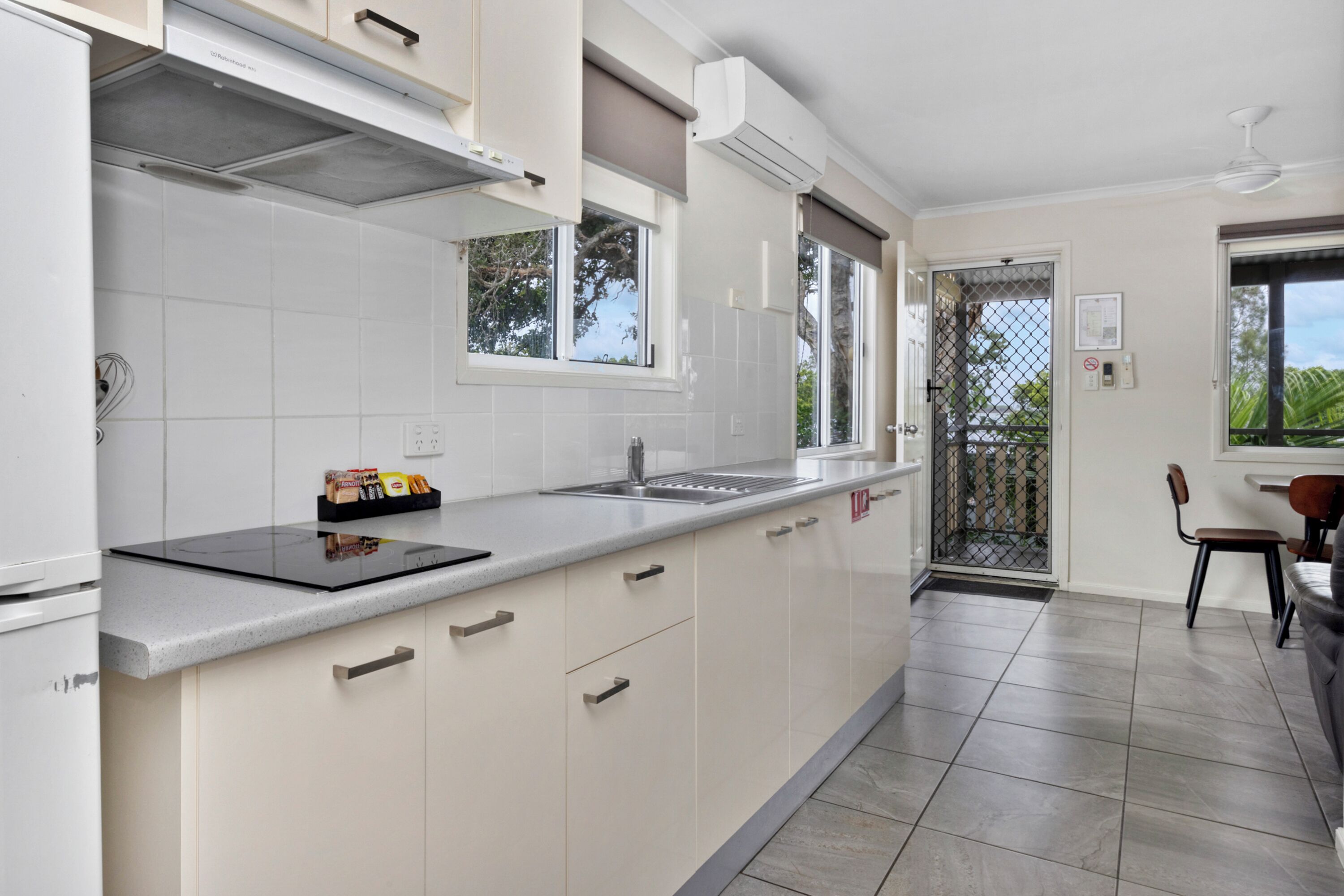 Una cocina moderna con armarios blancos, encimera negra y estufa integrada. Hay una ventana que ofrece luz natural y vistas al exterior.