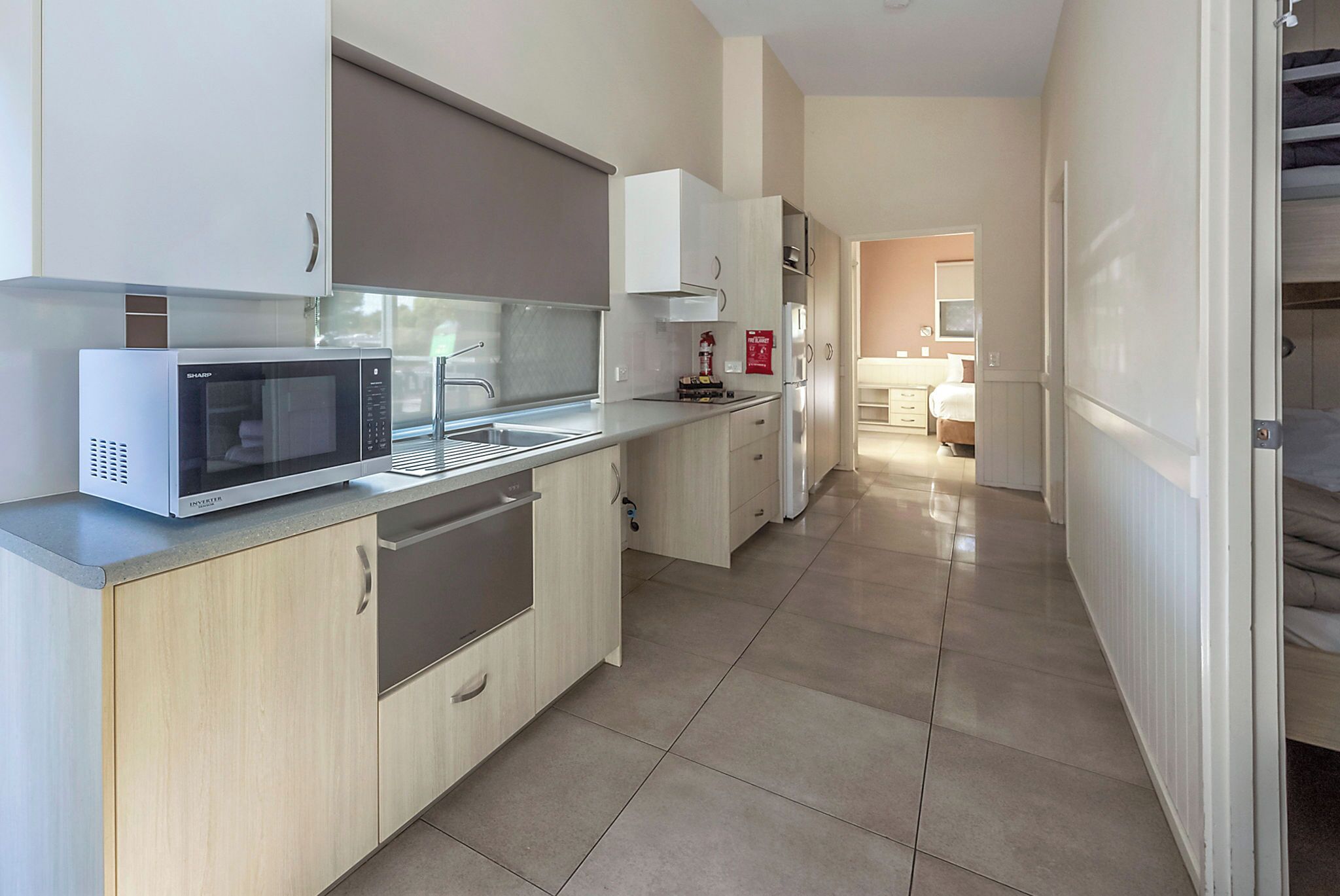Une cuisine moderne équipée d’un four à micro-ondes, d’un évier et de placards. Un couloir mène à une chambre à coucher qui comprend un lit et une commode.