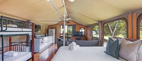 A tented accommodation with bunk beds, a kitchenette, and a seating area with a view of the outdoors.