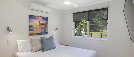 Un dormitorio con cama, ventana, ventilador de techo, aire acondicionado y un cuadro en la pared.