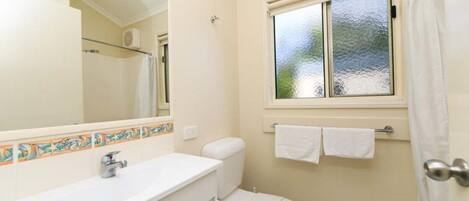 A bathroom with a toilet, a sink, a mirror, and a window with a view of trees.