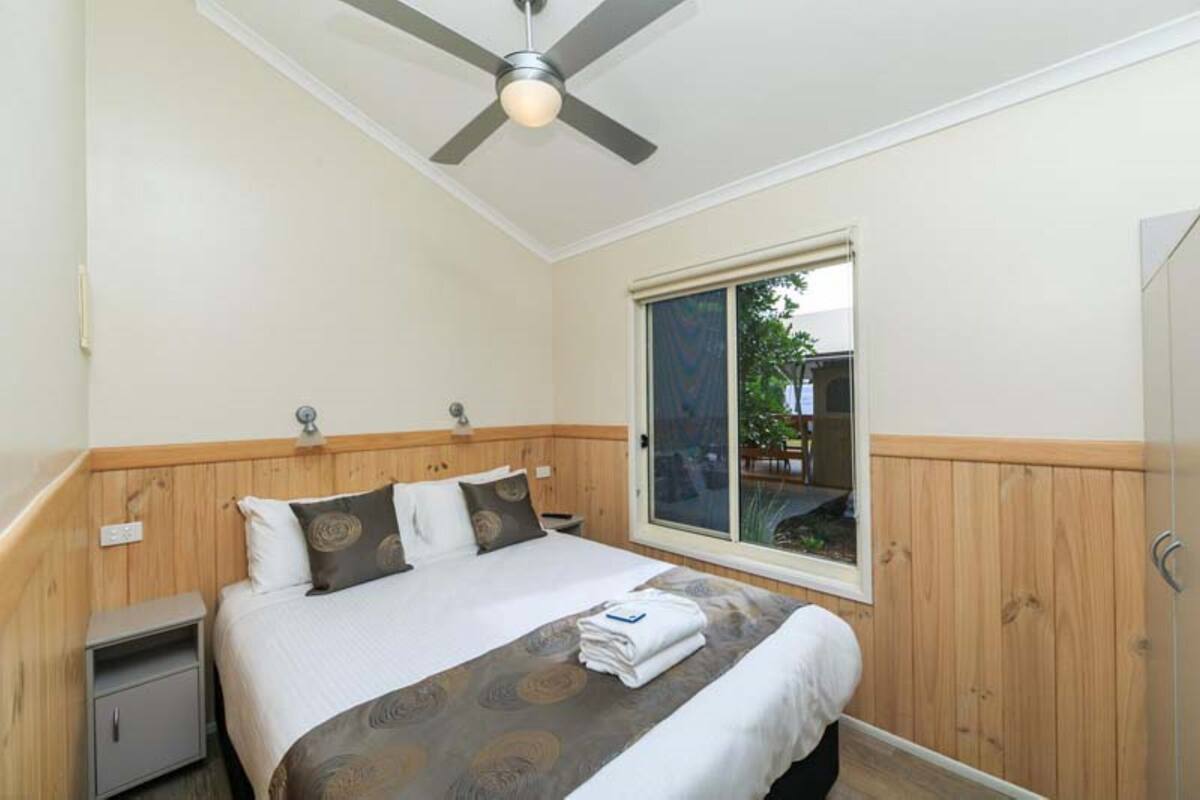 A bedroom with a bed, a nightstand, a ceiling fan, a window, and a wardrobe.