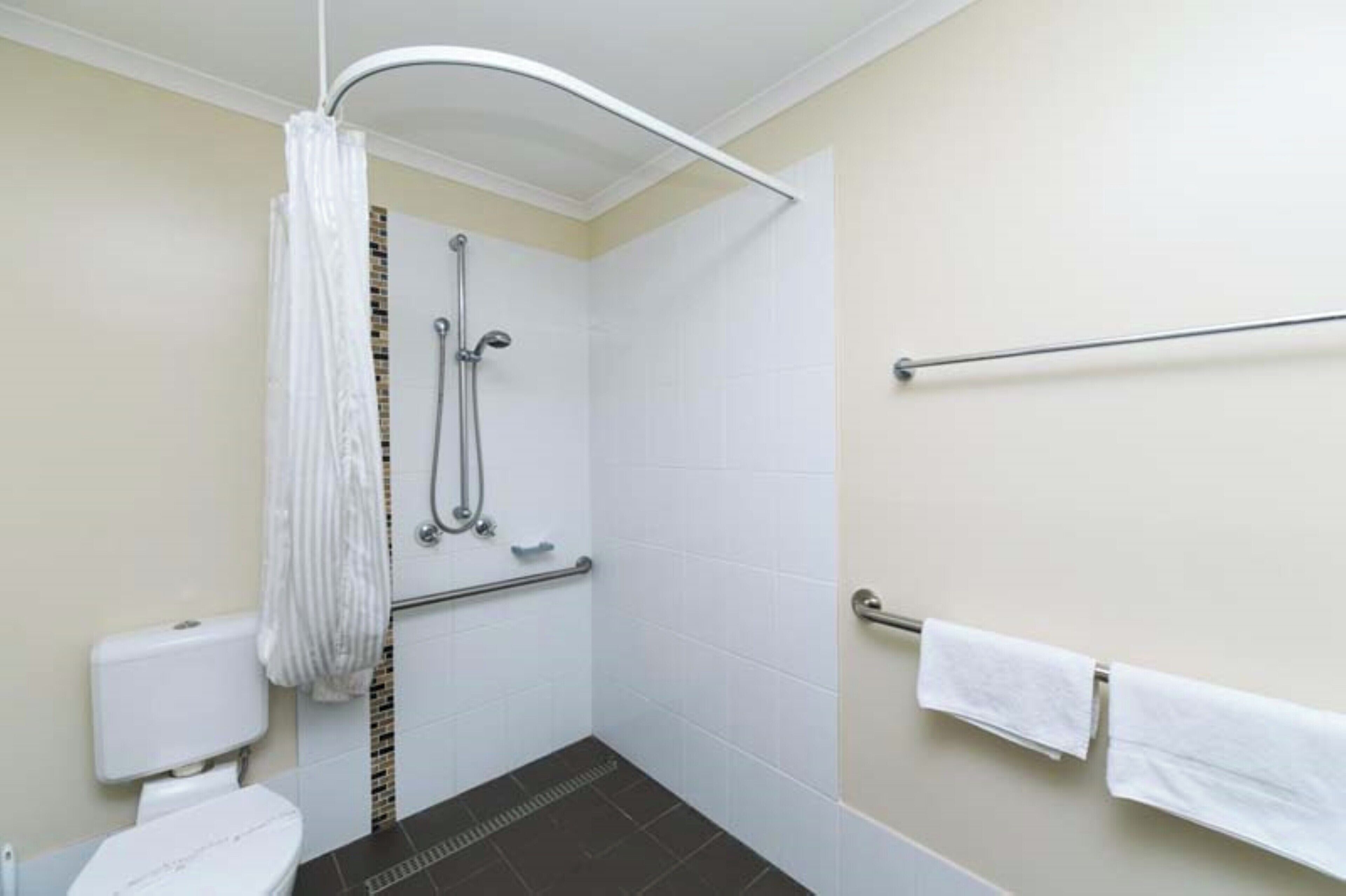 A small, modern bathroom with a shower, grab bars, and a toilet.