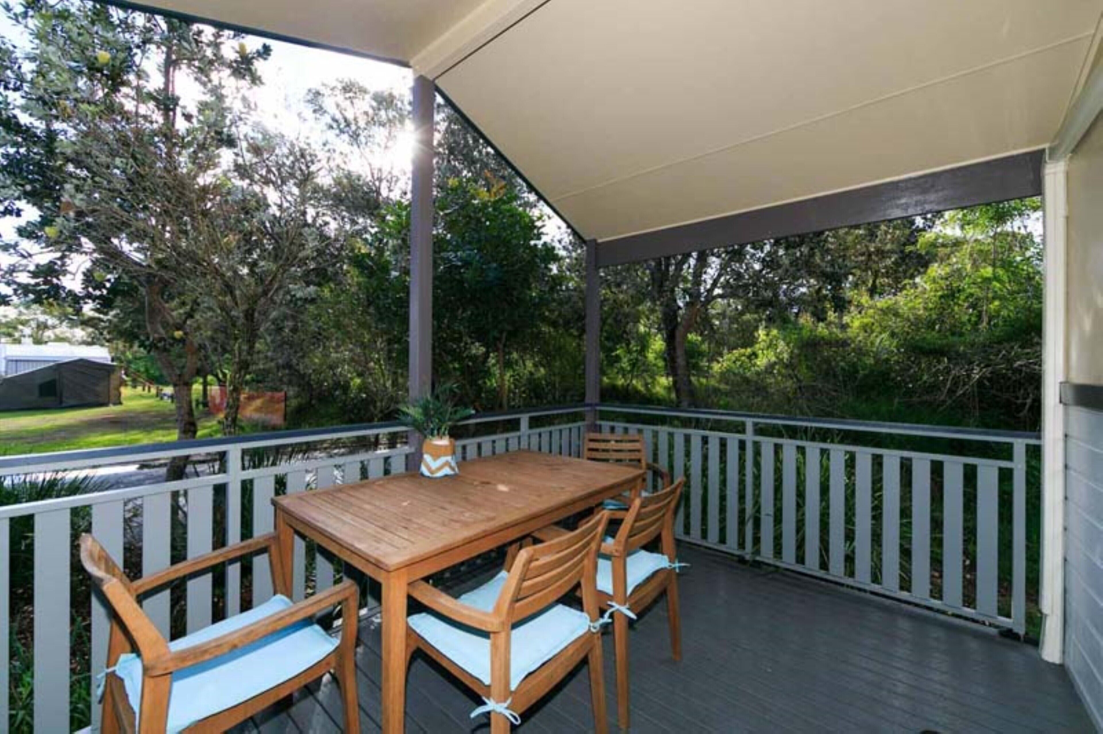 A covered outdoor patio with a wooden table and chairs, surrounded by a white picket fence.