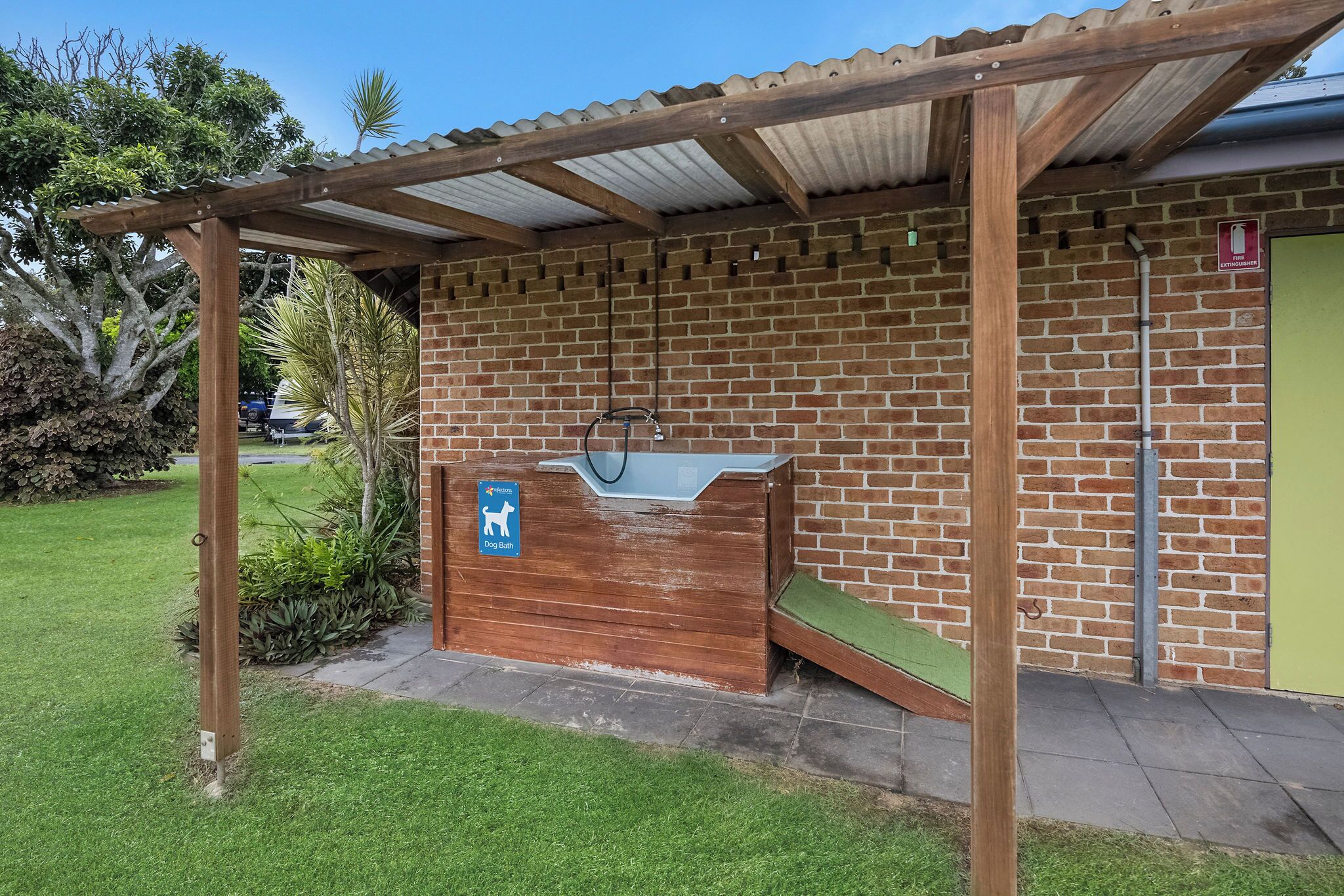 Espacio al aire libre apto para perros con un banco de madera, un bebedero para perros y una zona de estar cubierta.