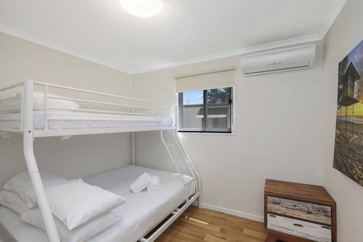 A bunk bed room with a window, an air conditioner, and a small wooden side table.