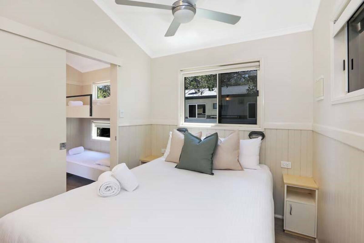A bedroom with a bed, a ceiling fan, a window, and a nightstand.