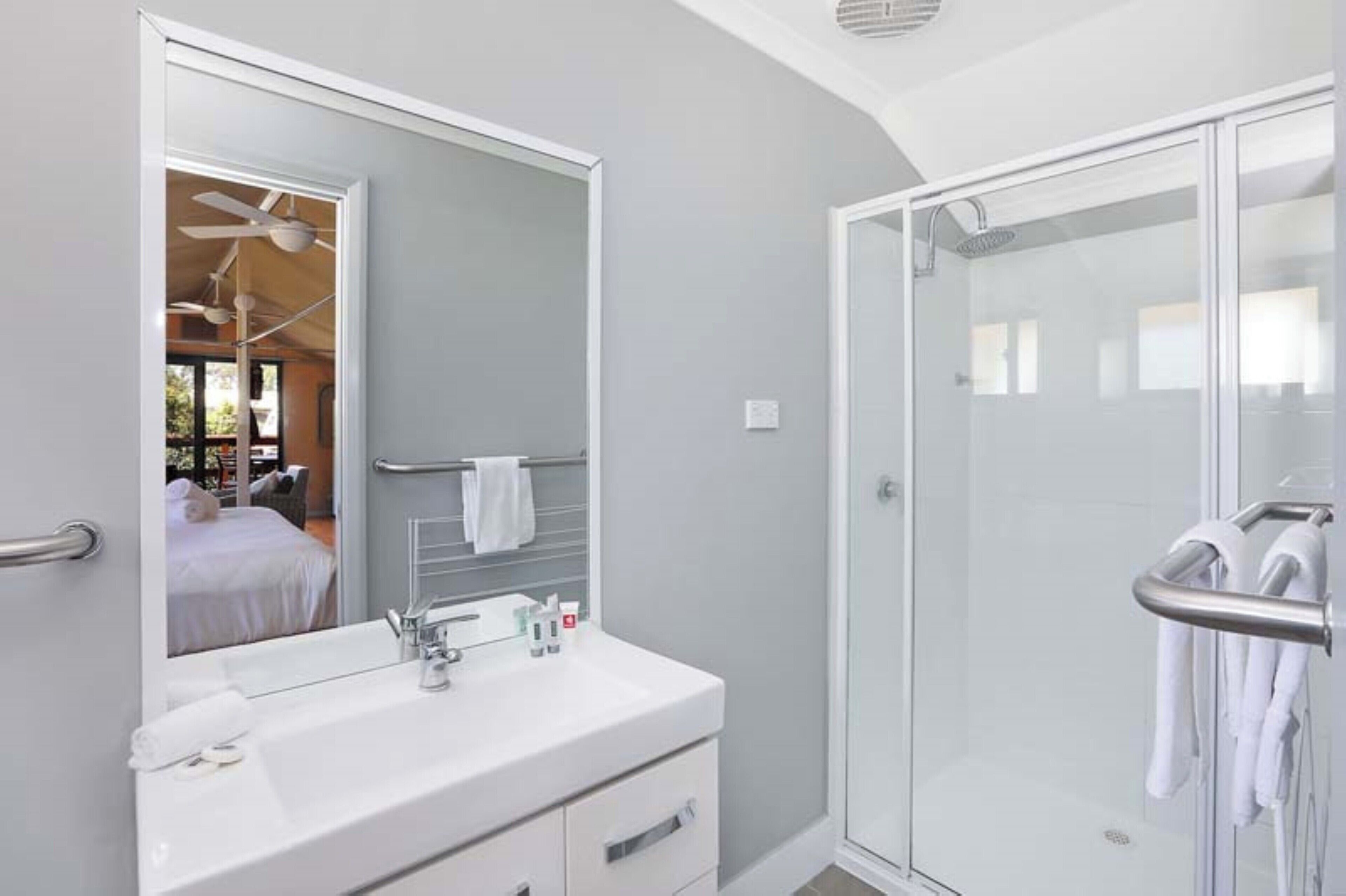 Een moderne badkamer met een grote spiegel, een witte wastafel en een douchecabine van glas.