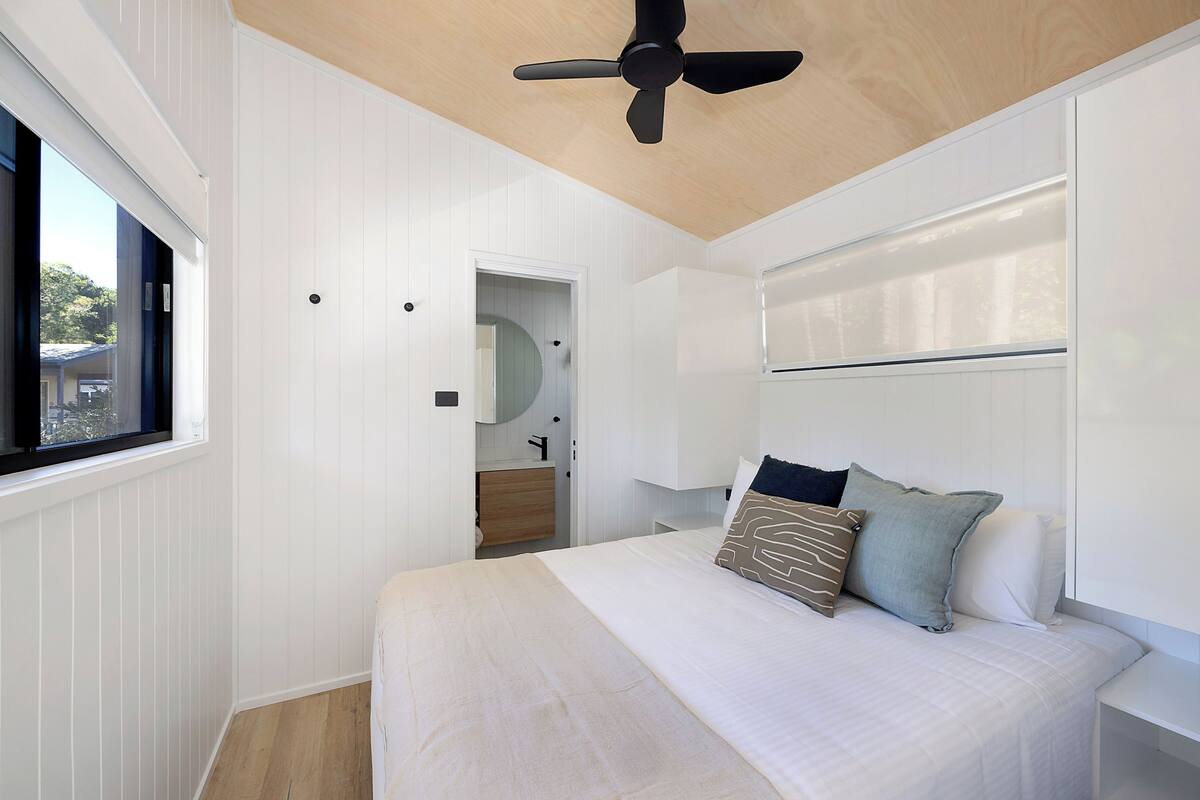 A bedroom with a bed, pillows, a ceiling fan, a window, and a door leading to a bathroom.