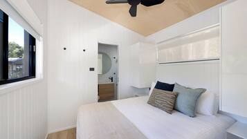 A bedroom with a bed, pillows, a ceiling fan, a window, and a door leading to a bathroom.