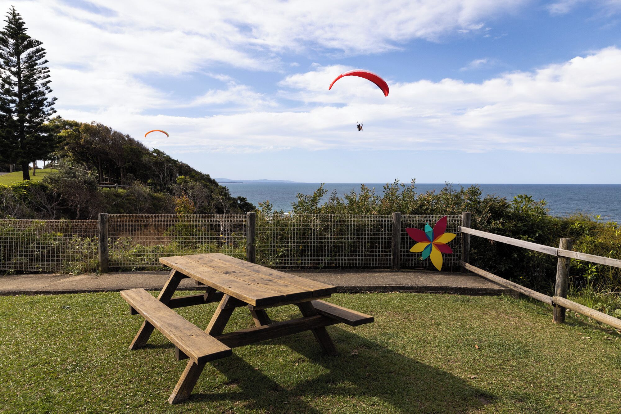 A picnic table in a grassy area with a view of the sea and a pinwheel decoration.