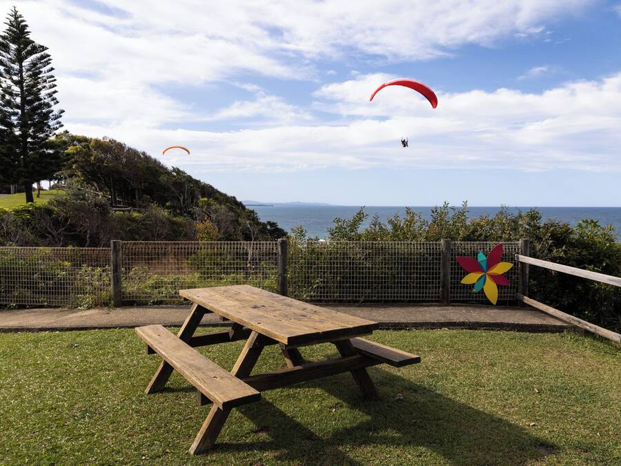 A picnic table in a grassy area with a view of the sea and a pinwheel decoration.