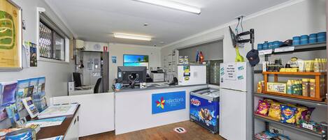 A reception area with a counter, a refrigerator, a television, and a shelf with snacks.