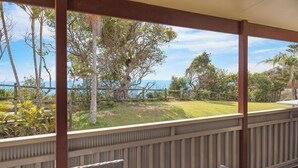 A covered outdoor area with a view of the sea, a grassy lawn, and a wooden fence.