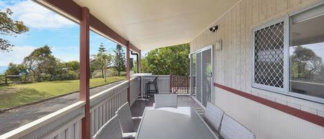 A covered patio with a table and chairs, a view of the surrounding greenery, and a window with a security screen.