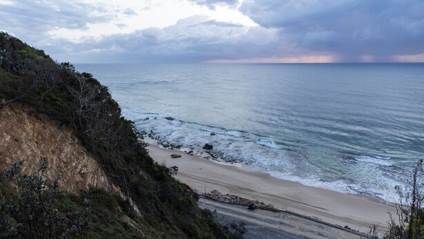 A coastal landscape with a beach, rocky shoreline, and vegetation.