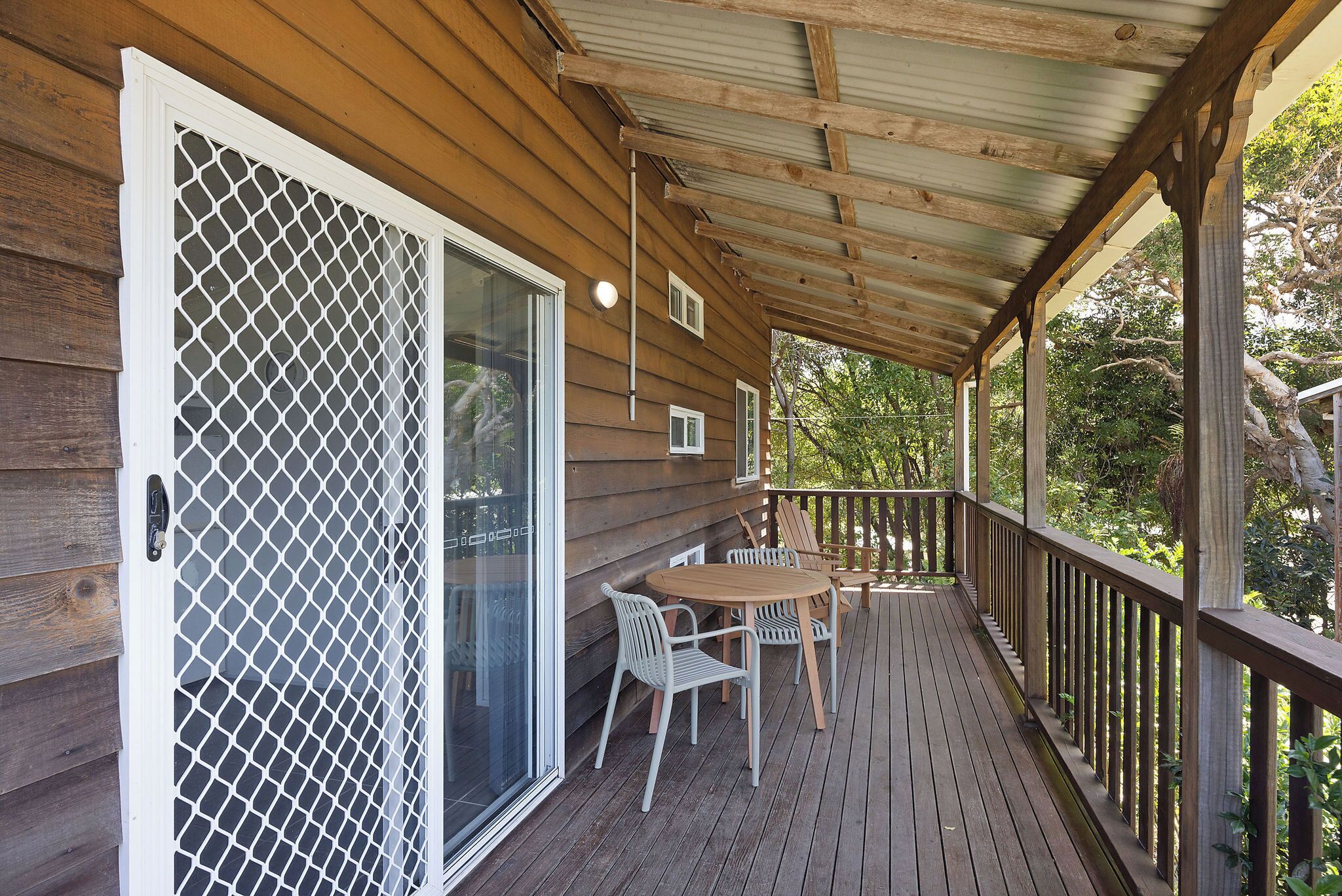 A wooden deck with a covered area, a sliding glass door with a security screen, and a table with chairs.