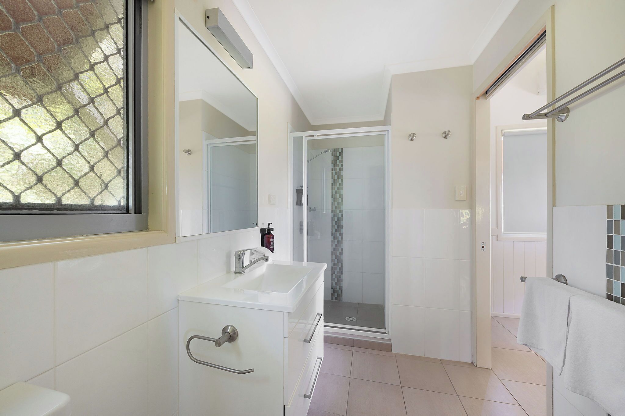 Un baño moderno con ducha de vidrio, azulejos blancos y un espejo grande.