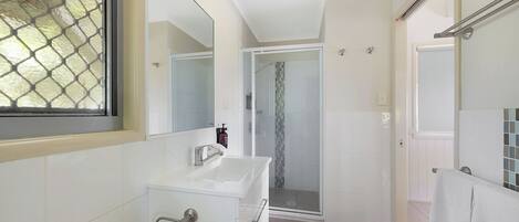 Un baño moderno con ducha de vidrio, azulejos blancos y un espejo grande.