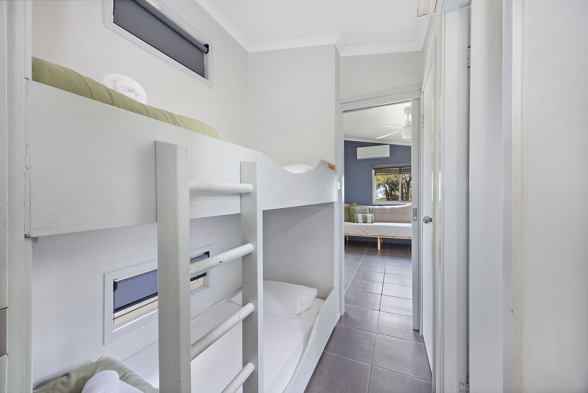 A corridor with bunk beds, a window, and a door leading to a room with a bed and a window.