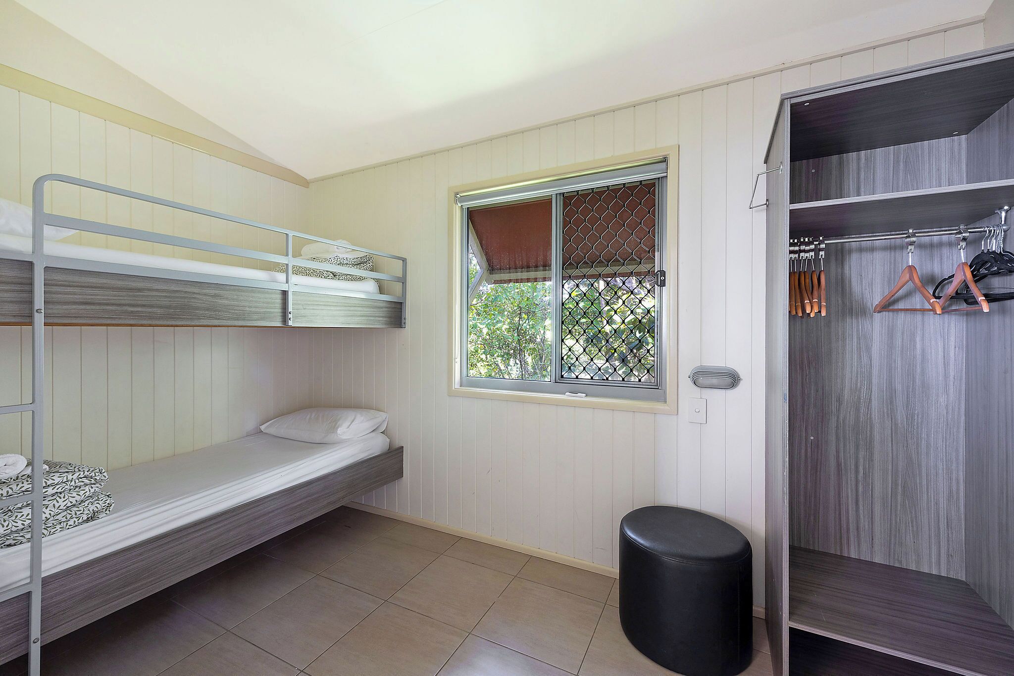 A dormitory room with bunk beds, a window, a closet, and a trash bin.