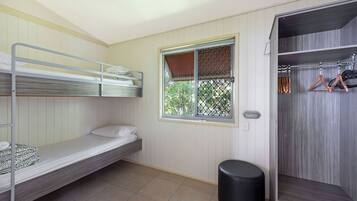 A dormitory room with bunk beds, a window, a closet, and a trash bin.