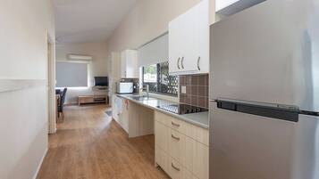 A modern kitchen with stainless steel appliances, light wood cabinets, and a wooden floor.