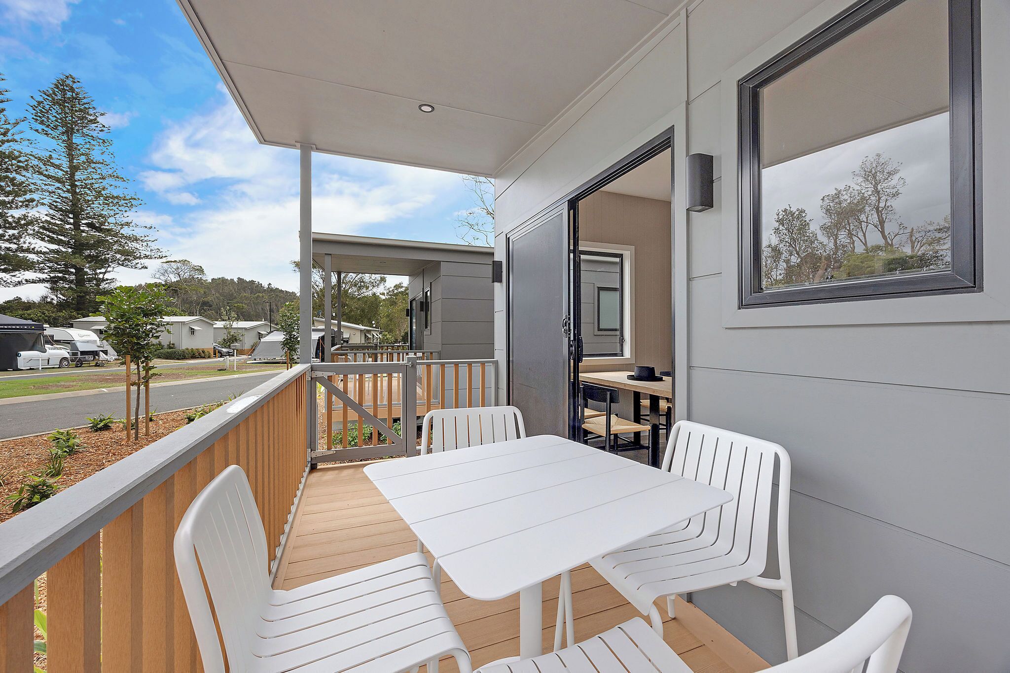 A covered outdoor area with a table and chairs, a wooden deck, and a view of the street and trees.