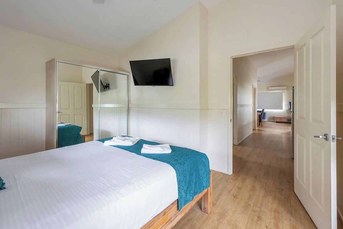 A hotel room with a bed, a TV mounted on the wall, and a mirror.