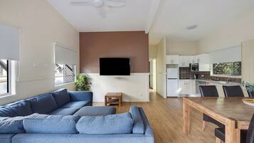 A modern living room with a grey sectional sofa, a wooden dining table, and a kitchen in the background.