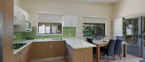 A modern kitchen with wooden cabinets, a white countertop, and a dining area with a table and chairs.