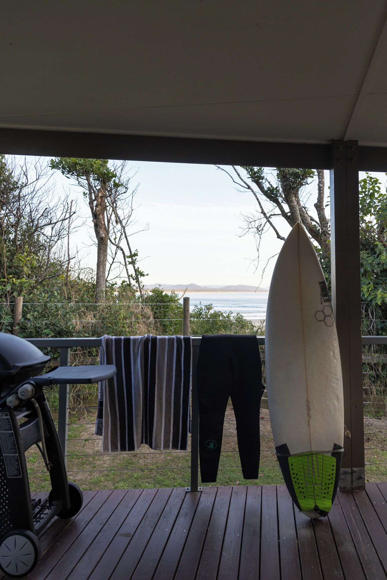 Un pontile in legno con una griglia, un'asse da surf e un asciugamano appesi a una ringhiera.