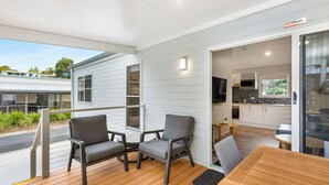 A modern outdoor deck with two grey chairs and a wooden table, connected to a white interior with a kitchen and a sliding glass door. - Reflections Scotts Head - Holiday Park (Scotts Head)