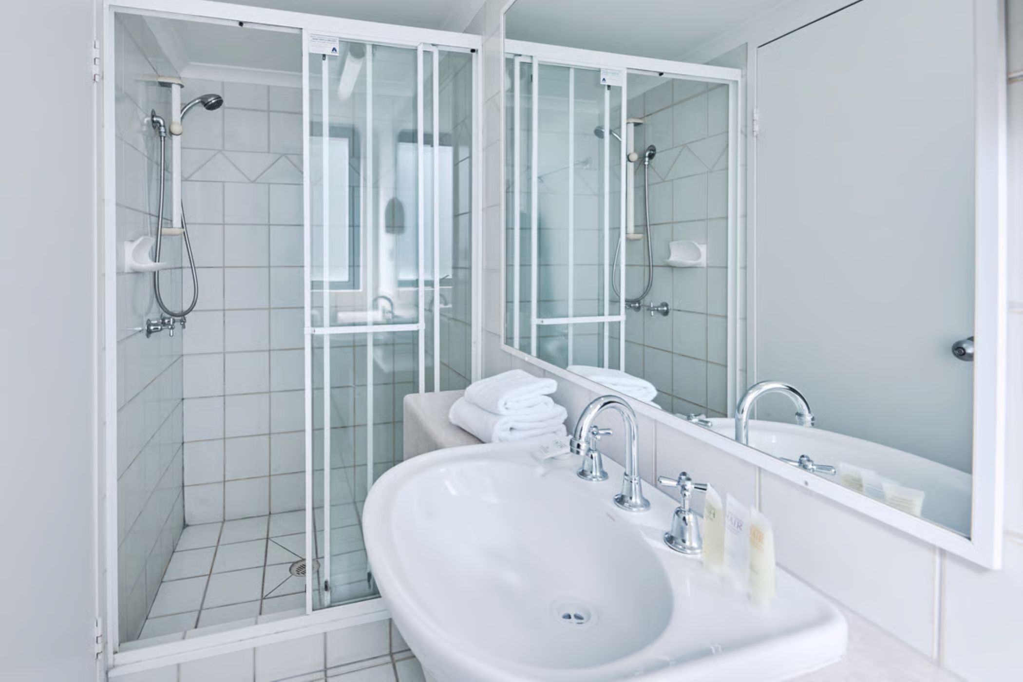 Une salle de bain moderne avec une douche à parois de verre, un lavabo blanc avec un miroir et des serviettes soigneusement rangées.