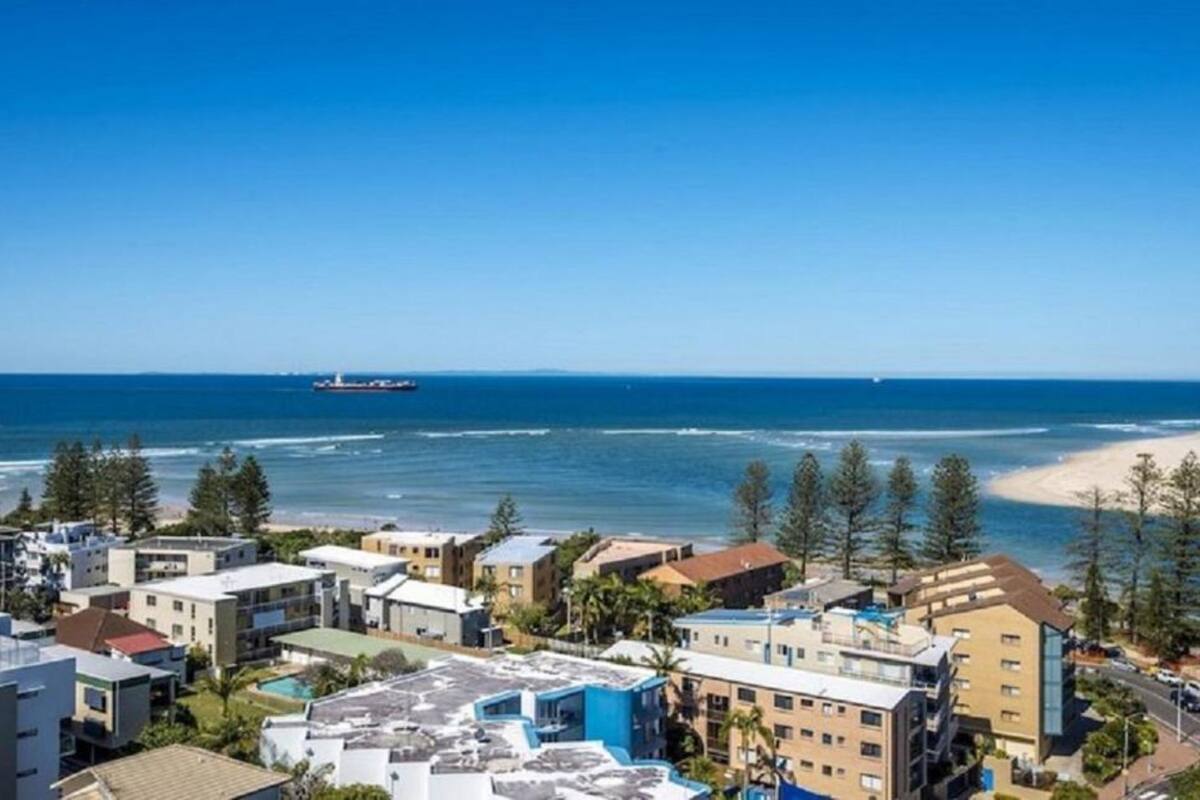 A coastal residential area with buildings, a beach, and a ship in the distance.