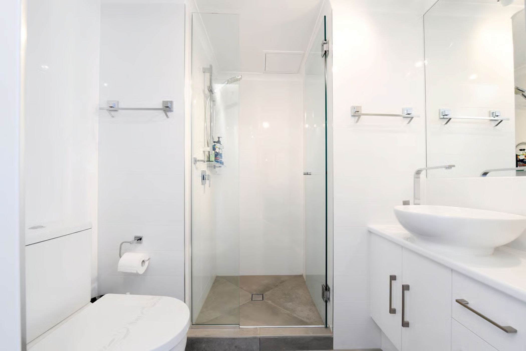 A modern bathroom with a glass shower enclosure, a white sink, and a marble toilet.