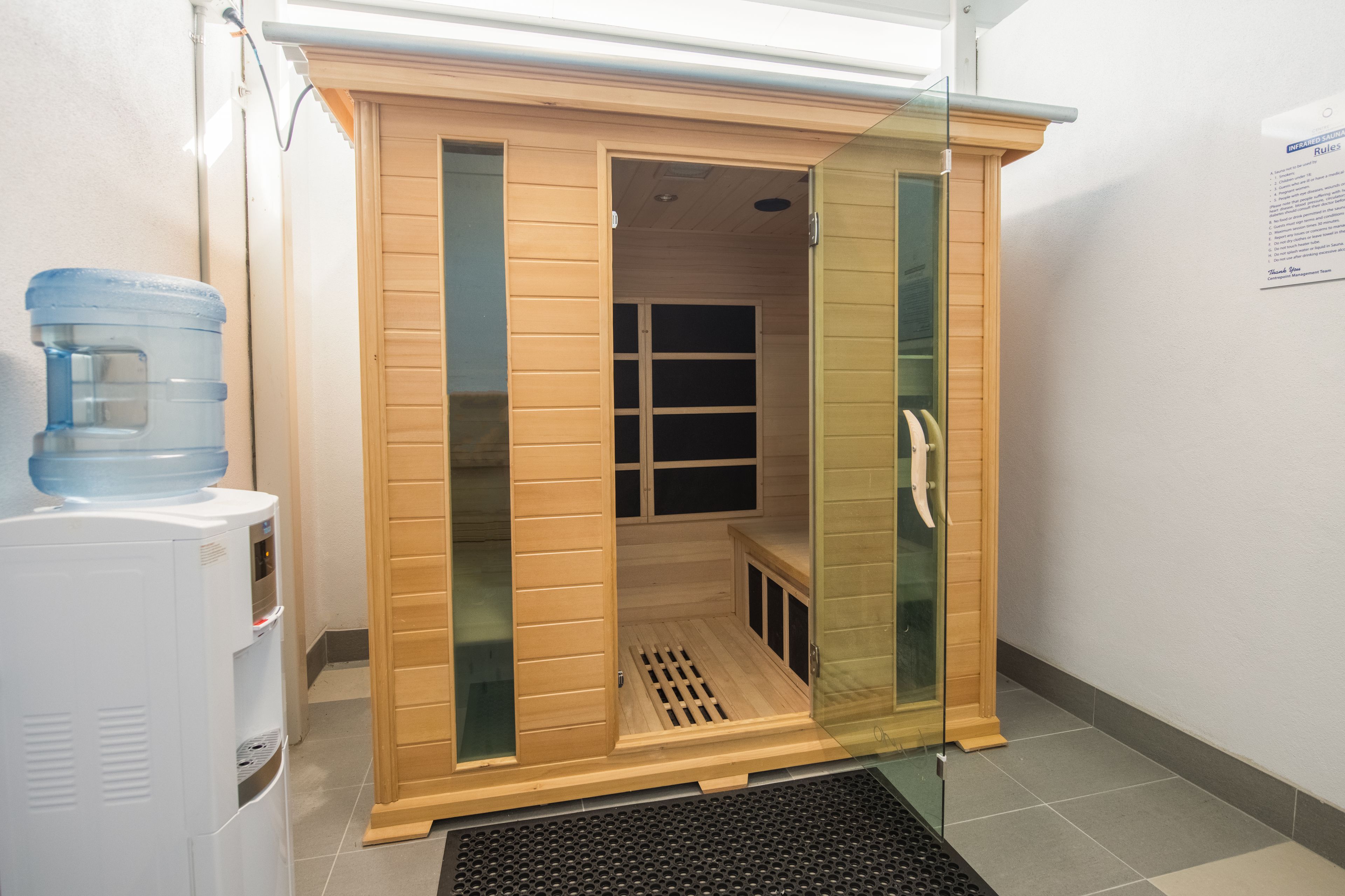 A sauna with a wooden exterior and glass doors, a water dispenser, and a tiled floor.
