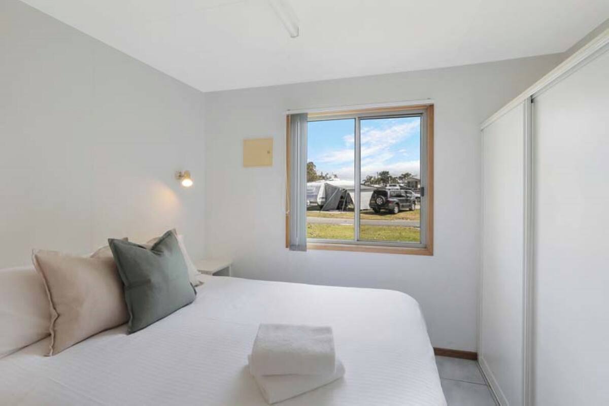 A bedroom with a large bed, a window with a view of parked cars, and a wall-mounted light.