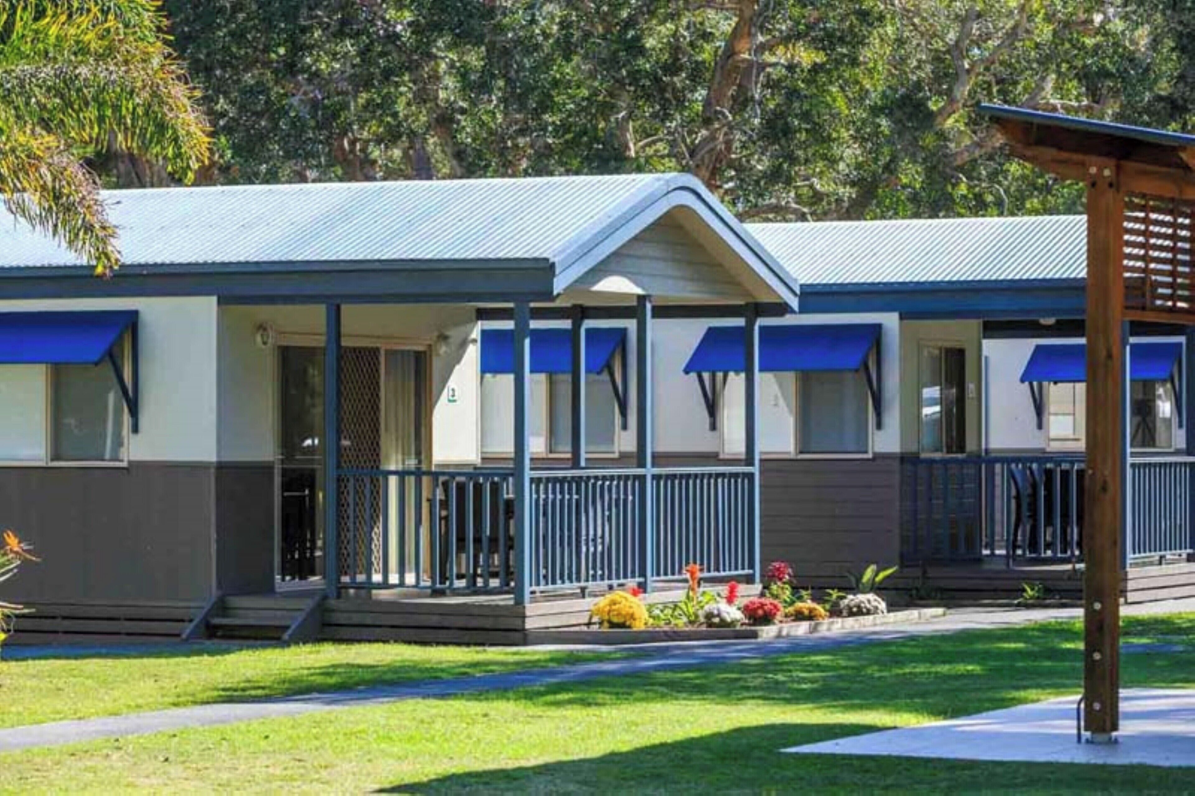 Een rij bungalows met blauwe luifels, een overdekte veranda en een verzorgd gazon.