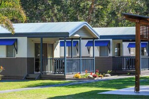 A row of single-story cabins with blue awnings, a covered porch, and a well-maintained lawn.
