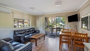 Un salón amplio con un sofá de cuero negro, una mesa de centro de madera y un comedor con sillas y mesa de madera.