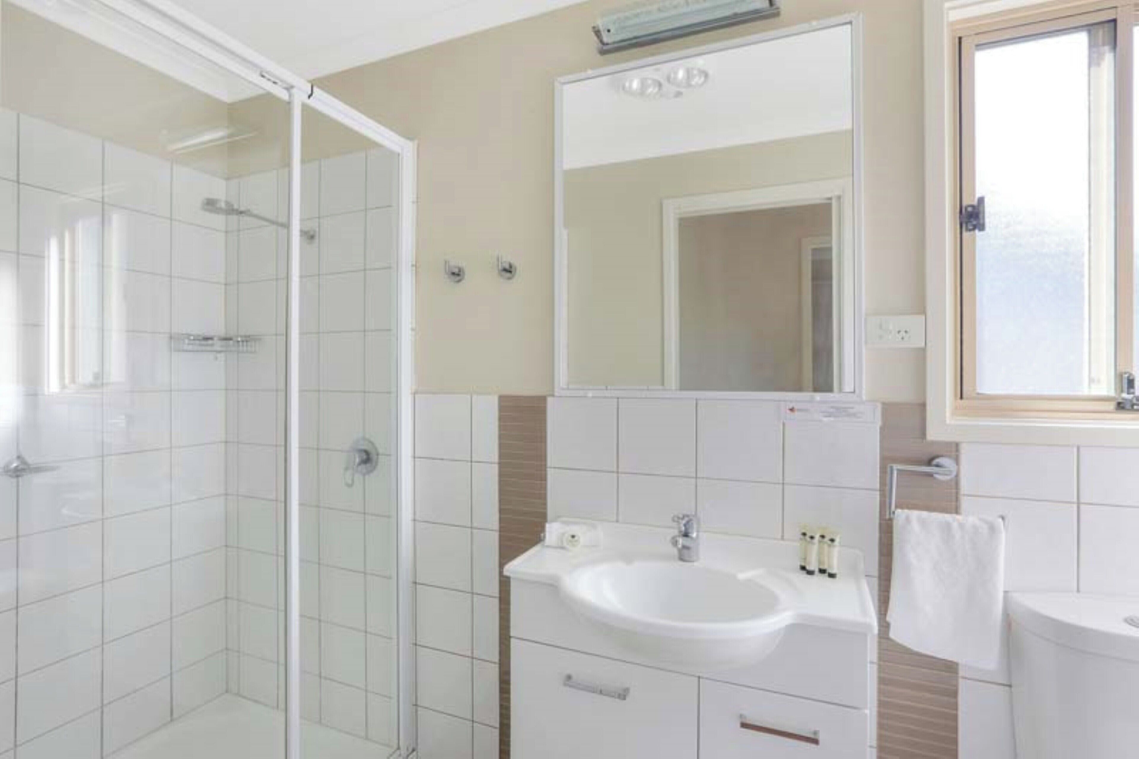 A modern bathroom with a glass shower enclosure, a white sink, and a mirror above it.