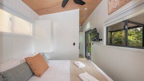 Un dormitorio con cama, almohadas, ventilador de techo y ventana con vistas a follaje.