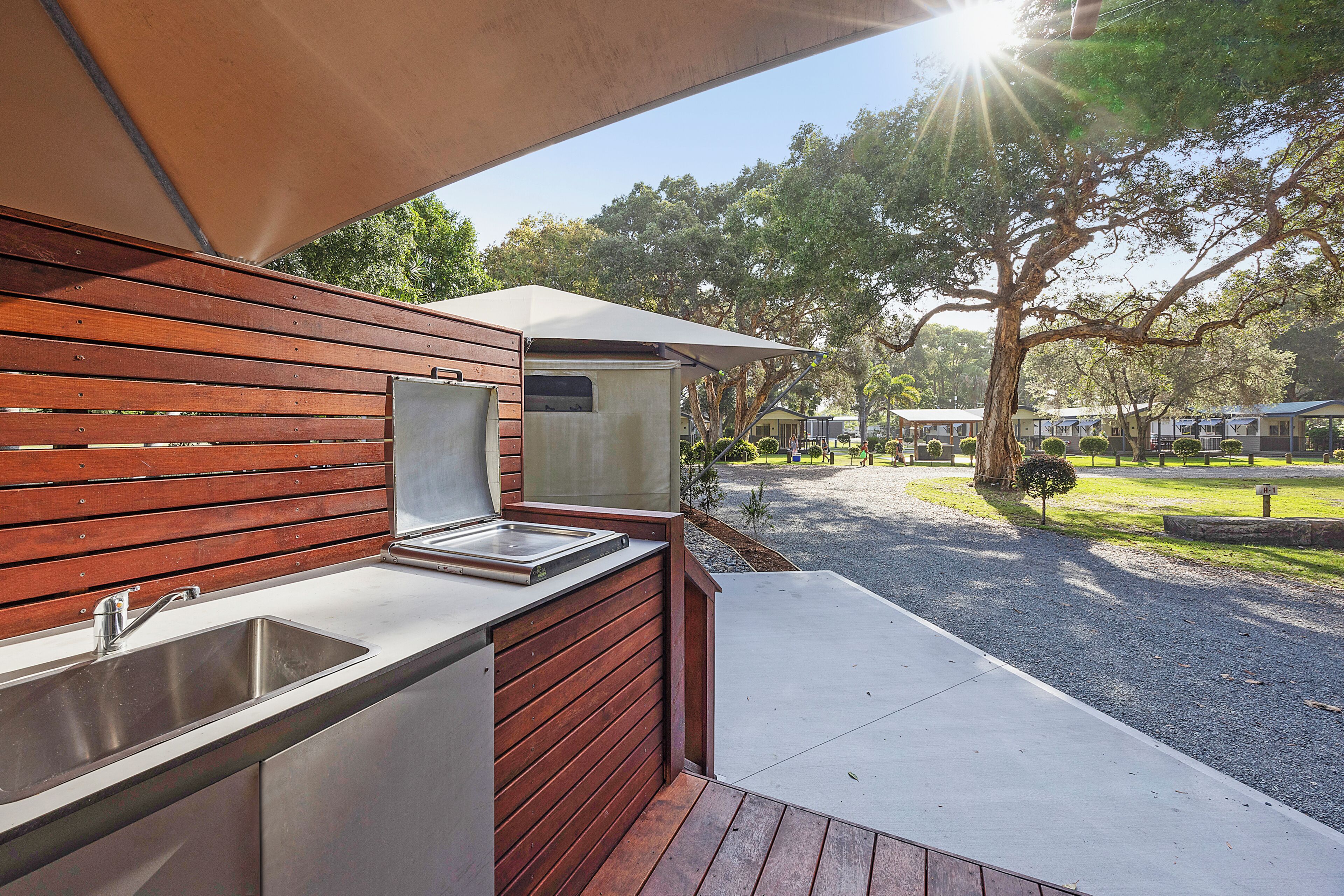 An outdoor kitchen area with a sink and a built-in oven, surrounded by wooden panels and a concrete floor.