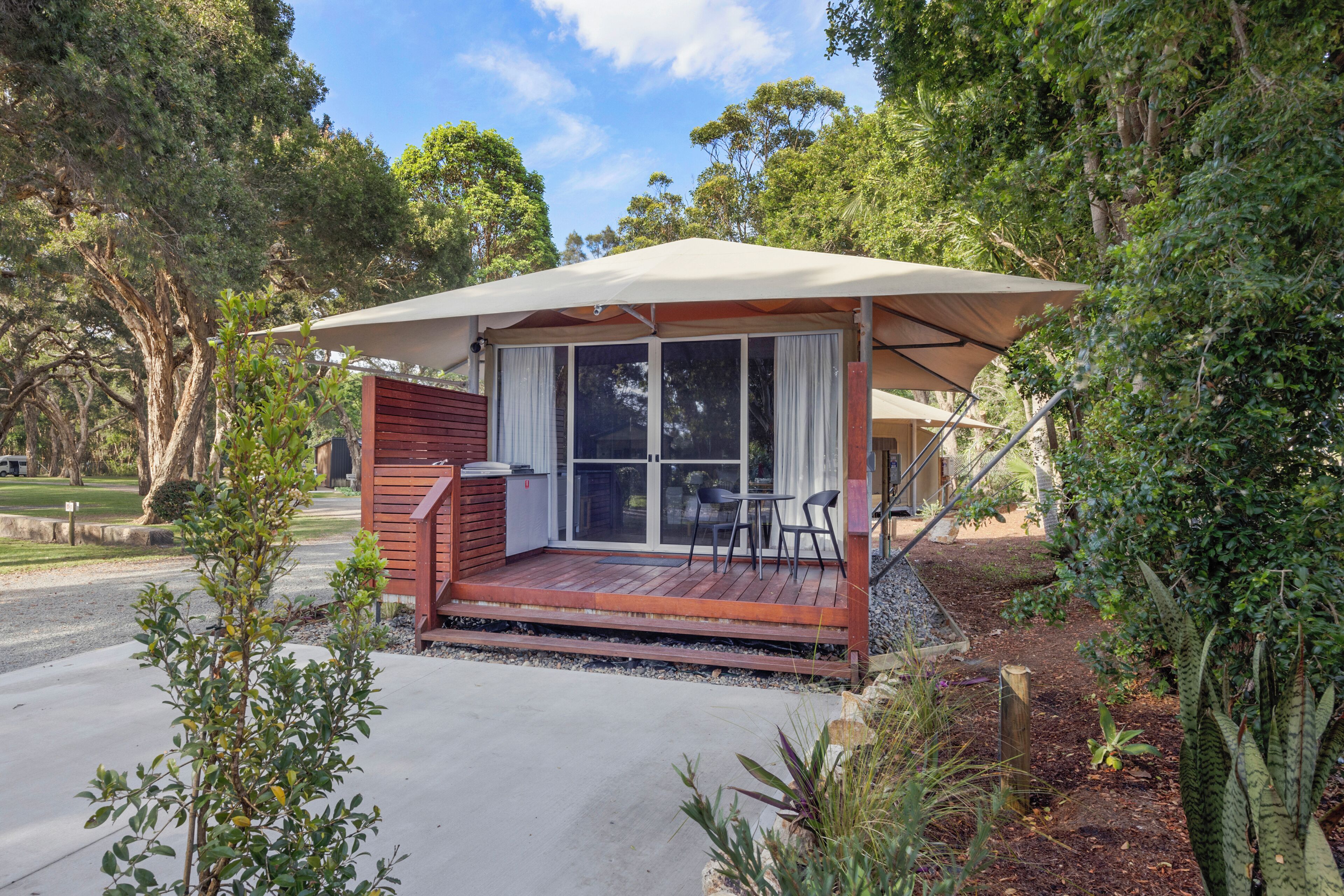 A small wooden cabin with a covered patio, a sliding glass door, and a seating area with two chairs.
